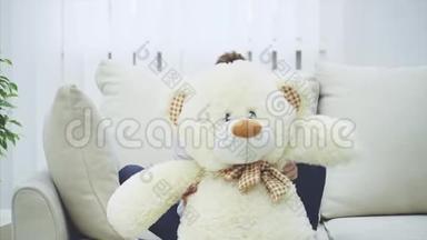 有趣的小女孩躲在白色的泰迪熊后面，挥动它的爪子，然后出现并拥抱它。